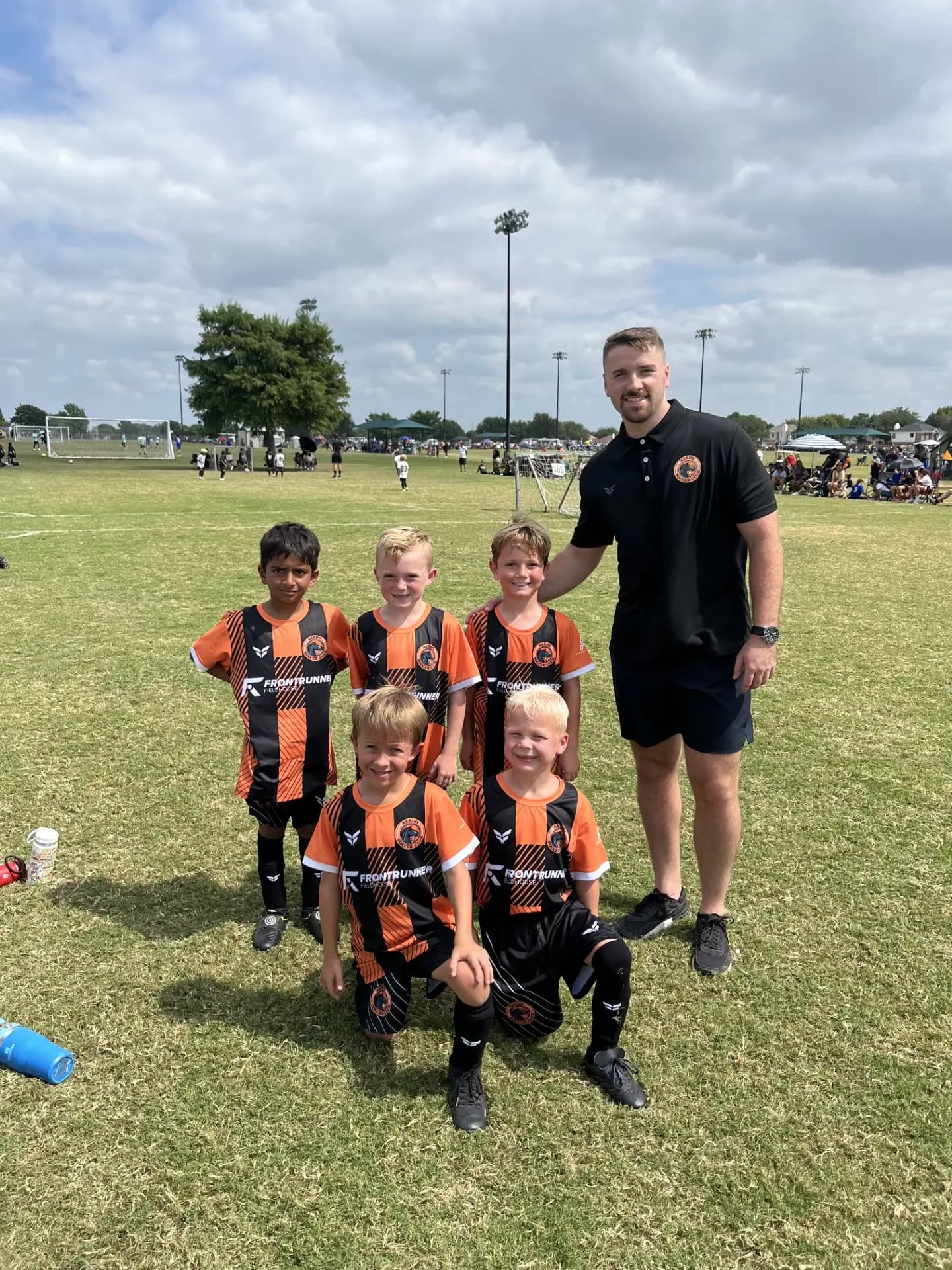 A young Aledo Soccer Club 4v4 team in orange kits posing with their coach on game day
