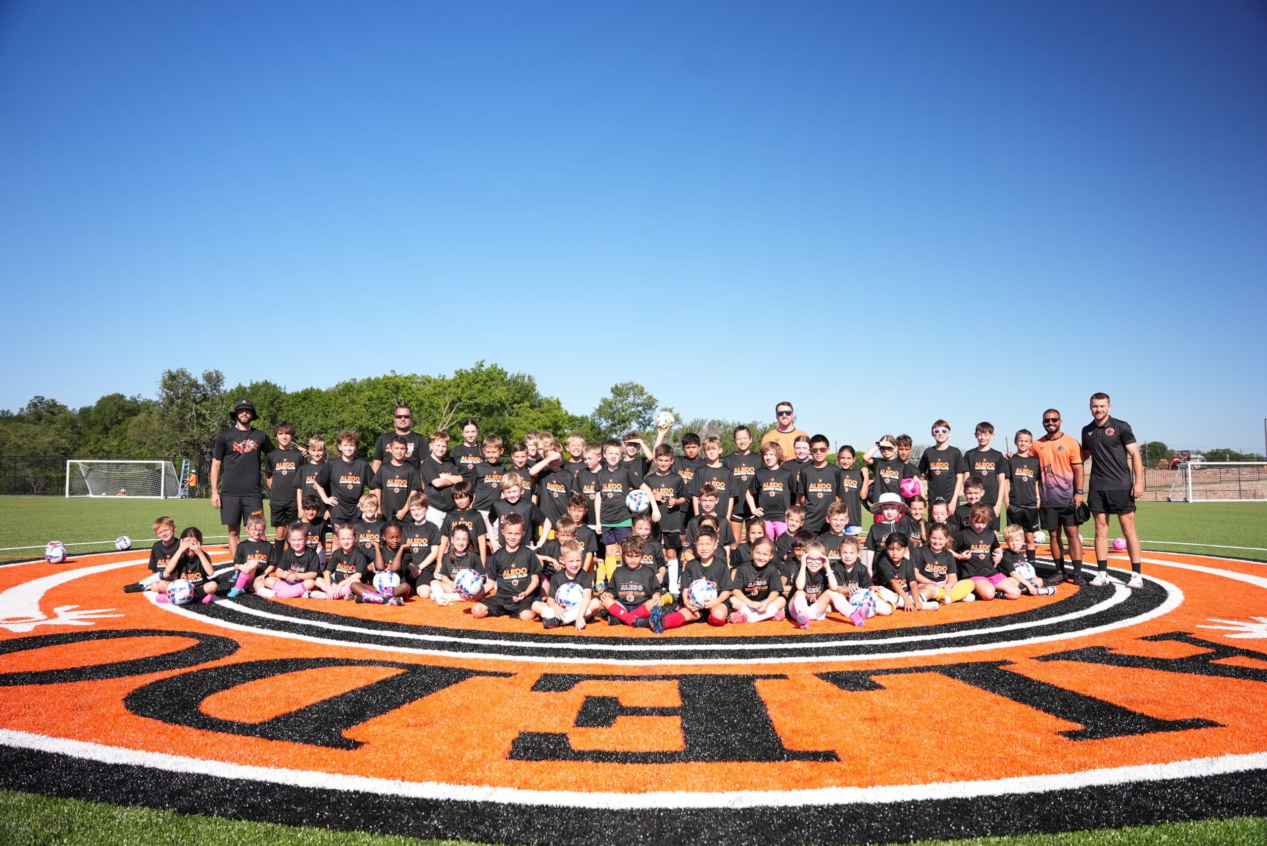 Aledo Soccer Club Summer Camp 2026 — coaches and campers on the center circle at The Stable