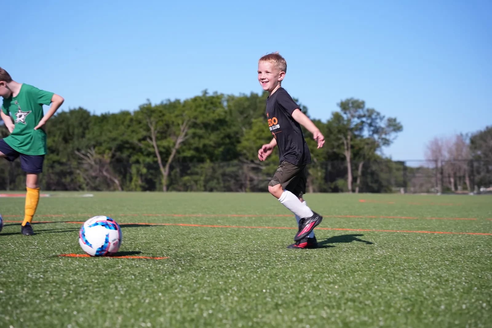 A grinning young Little Aledos player chasing the ball across the field at The Stable